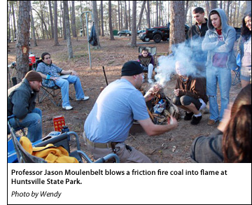 Professor Jason Moulenbelt blows a friction fire coal into flame at Huntsville State Park