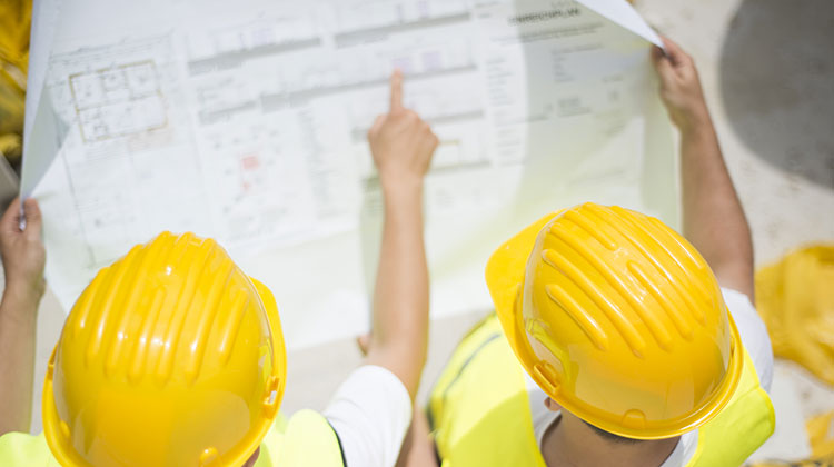 Two people wearing hard hats while inspecting plans