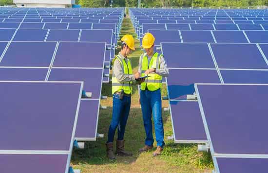 Two people in hard harts standing among solar panels