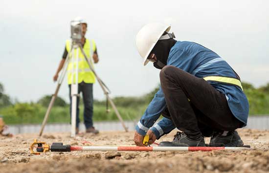 Two workers using land surveying tools