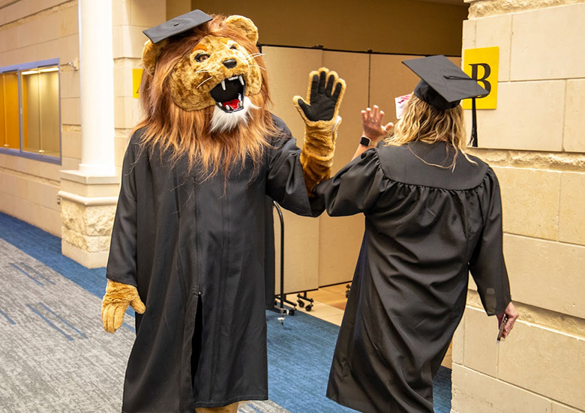 LSC-University Park Leo Mascot High-Fiving Student in Graduation Robe