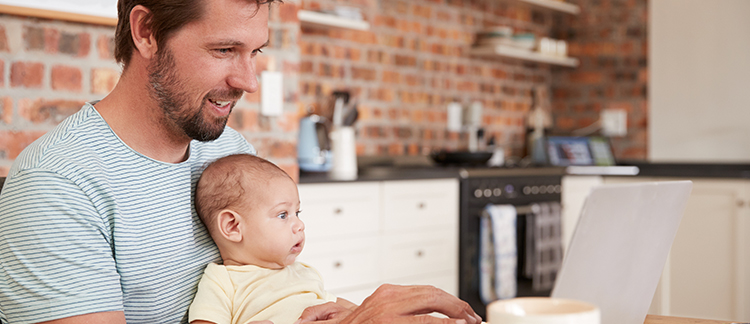 Man at home using computer with baby in his lap