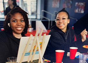 Two female students smiling and painting 