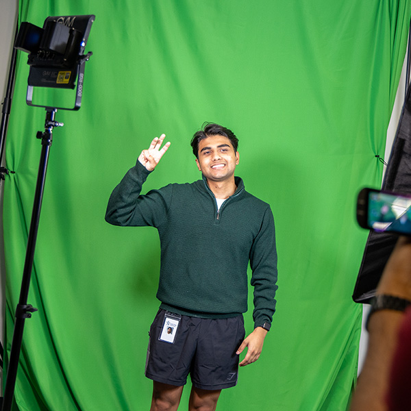 Student posing in front of a green screen