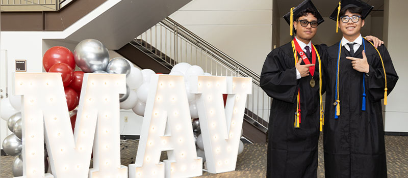 two male students graduation with mav sign
