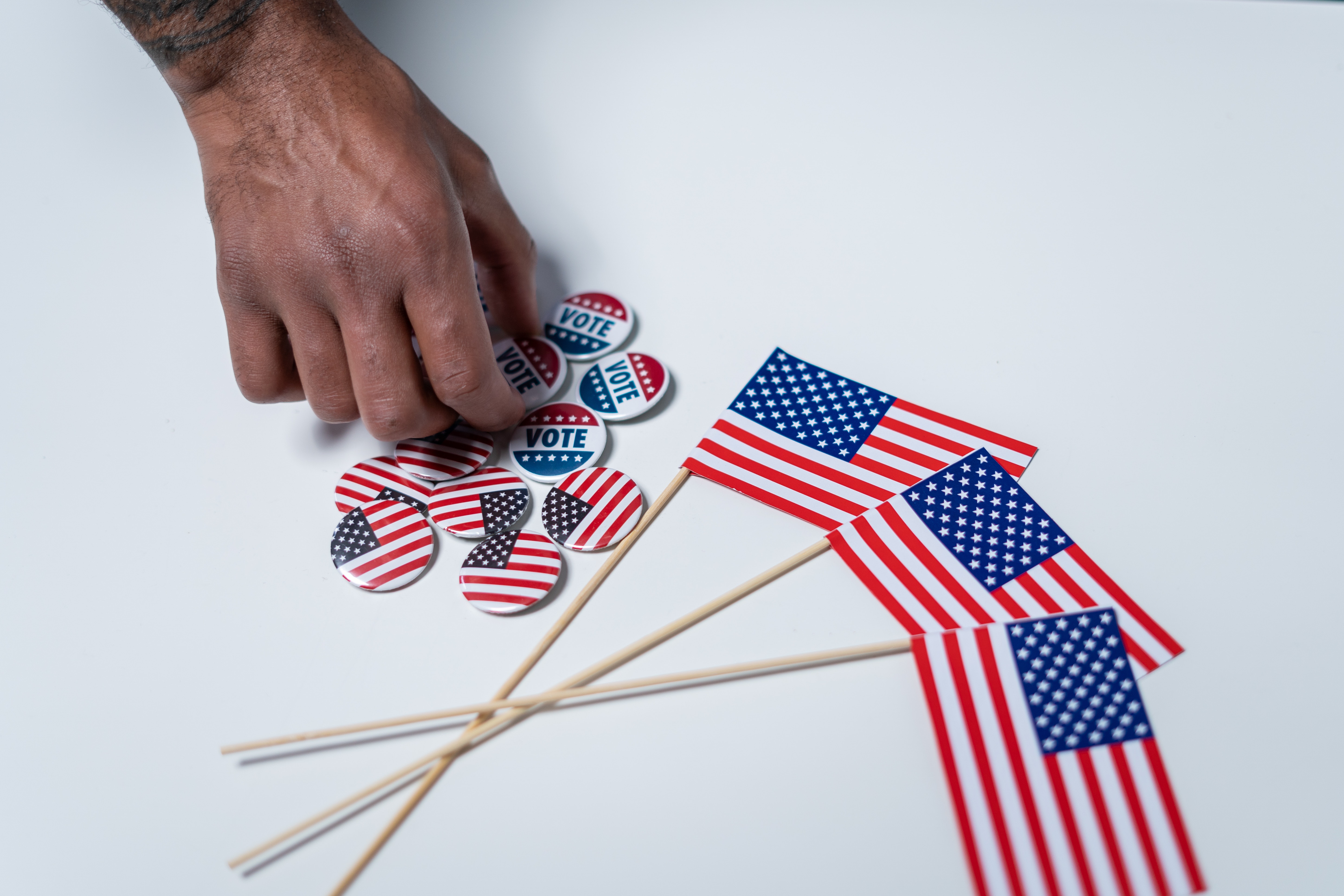 Hand Picking Up Vote and American Flag Buttons Next to Small Hand-Held American Flags