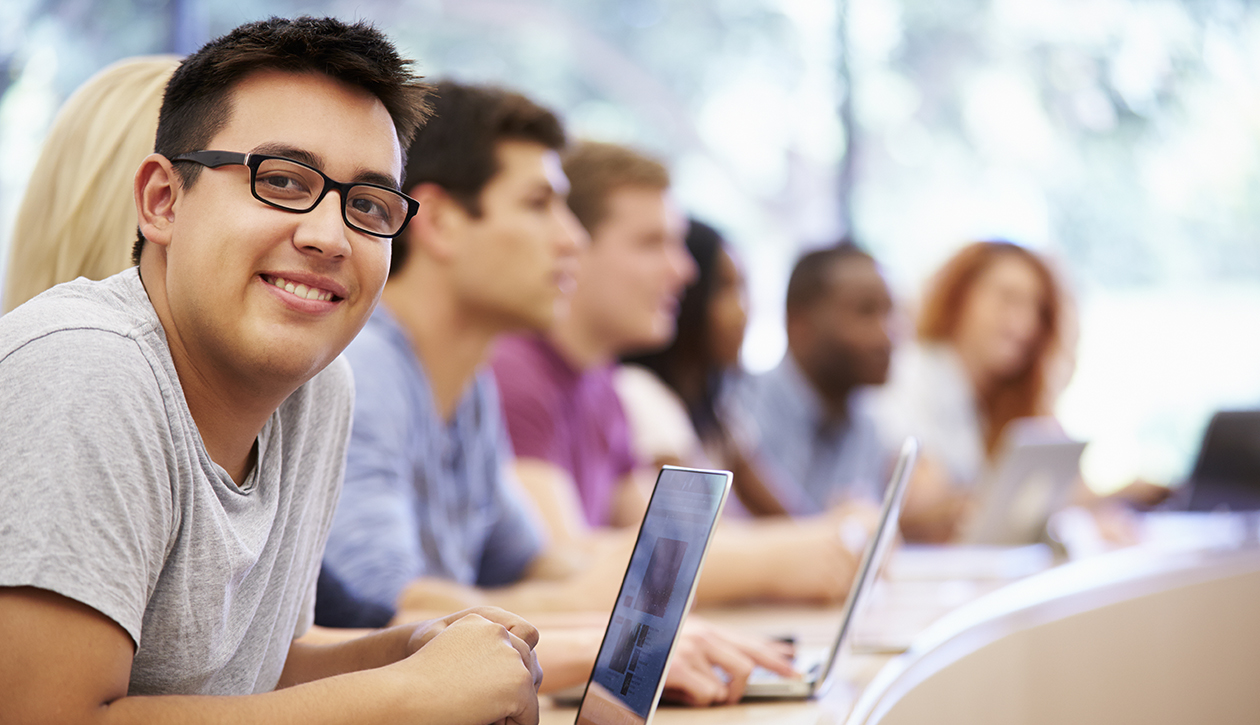 young hispanic male sitting in college classroom looking at camera