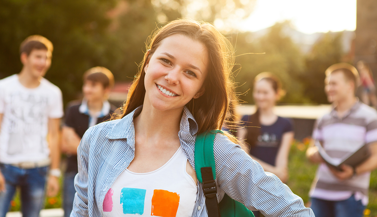 Young white female with backpack standing in front of mixed group of college students