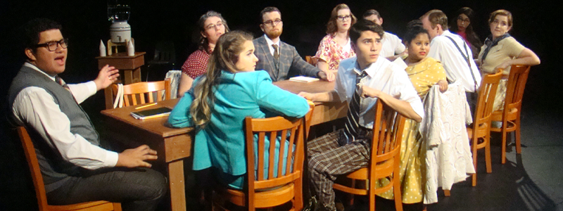 11 people sitting at a long table, wearing nice clothes. Most of them are looking out in the same direction.