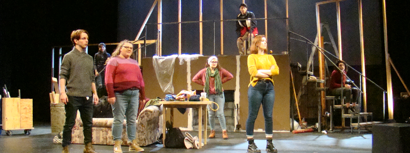 A group of people standing near scaffolding, a couch, and a small table.