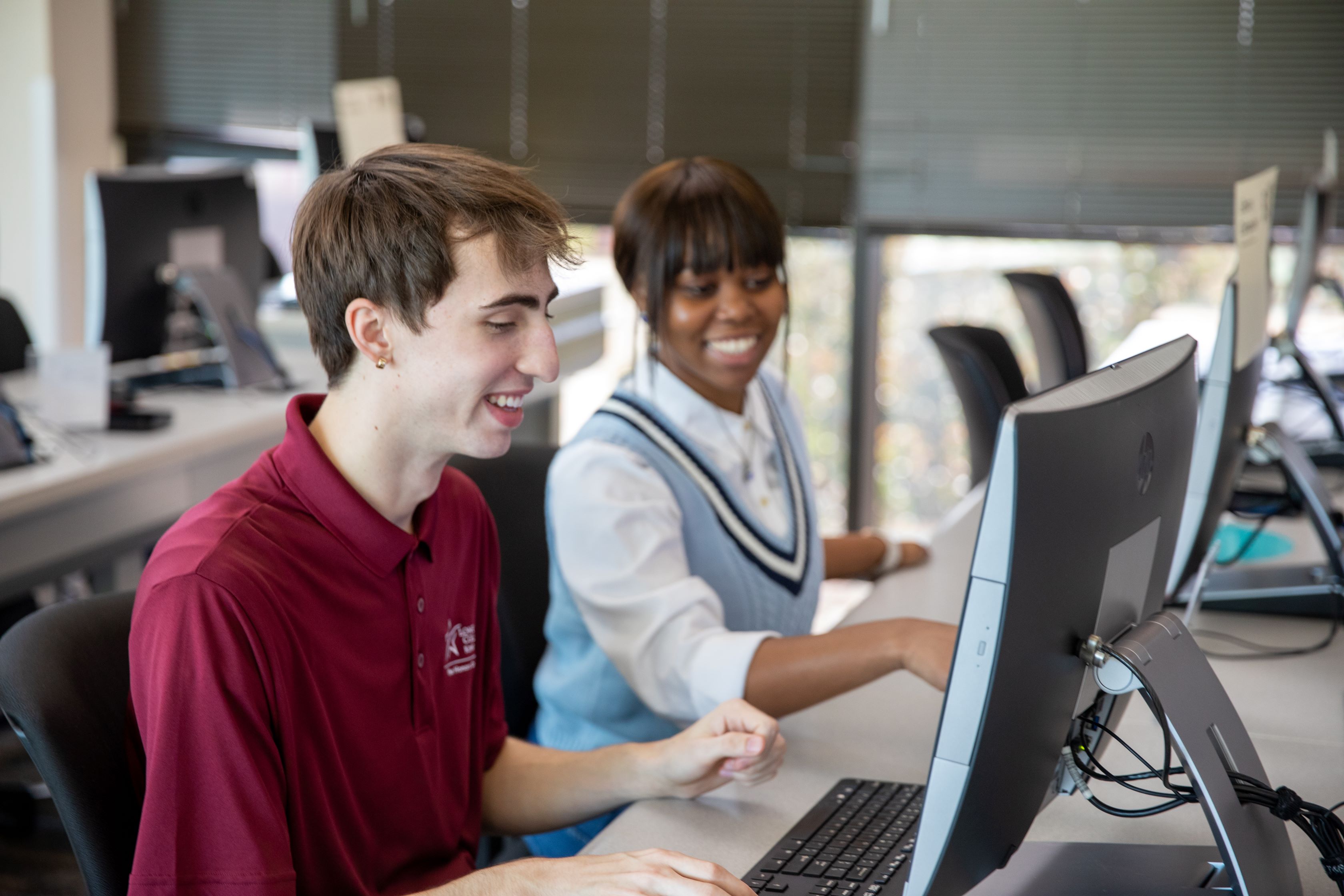 A student and Professor in a classroom looking at a computer. 