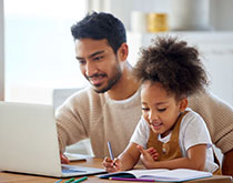 Man holding daughter while studying on laptop