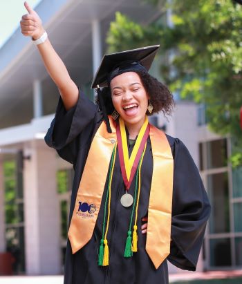 Student with cap and gown giving a thumbs up