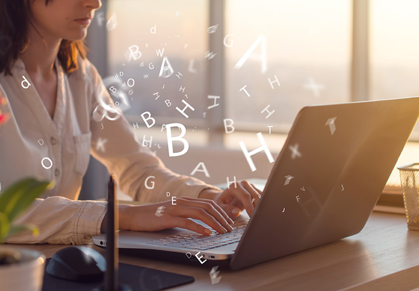 Woman typing on a laptop, with letters of the alphabet floating around her to show that she is writing