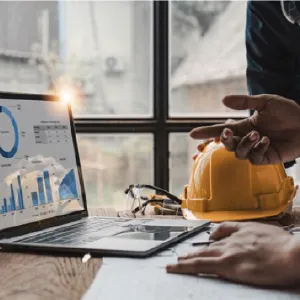 Laptop with graphs next to a hard hat