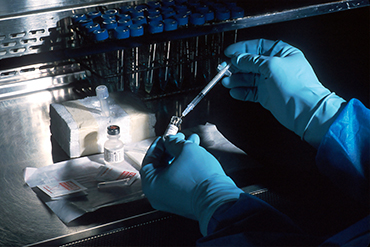 Gloved hands sticking a syringe into a vial