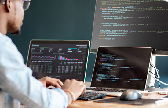 A man looking at code on multiple monitors