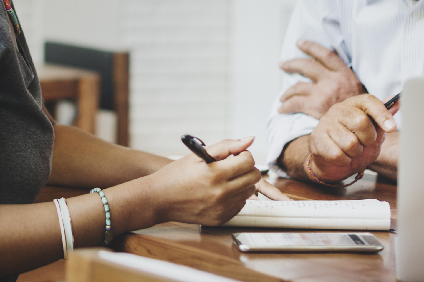 Two pairs of hands holding pens near notebook and calculator on table