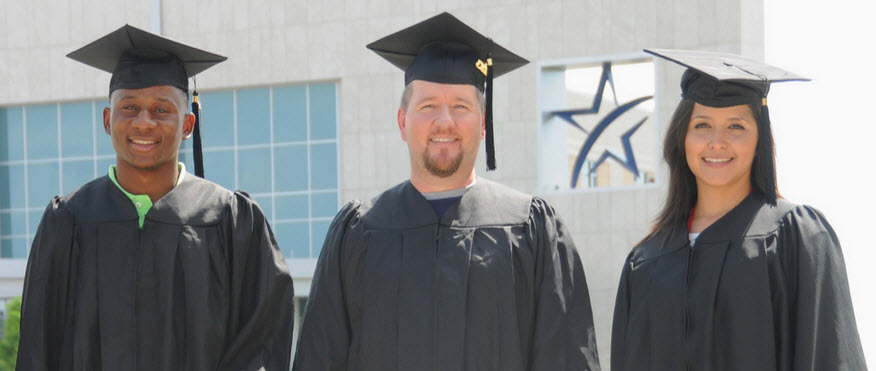 Three graduates in regalia with campus exterior in background
