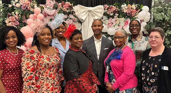Attendees and speakers pose for a group photo at the “Spill The Tea: The Evolution of Women Impacting Leadership” event at Lone Star College–North Harris. The group stands in front of a floral tea-party themed backdrop with pink balloons and greenery, cel