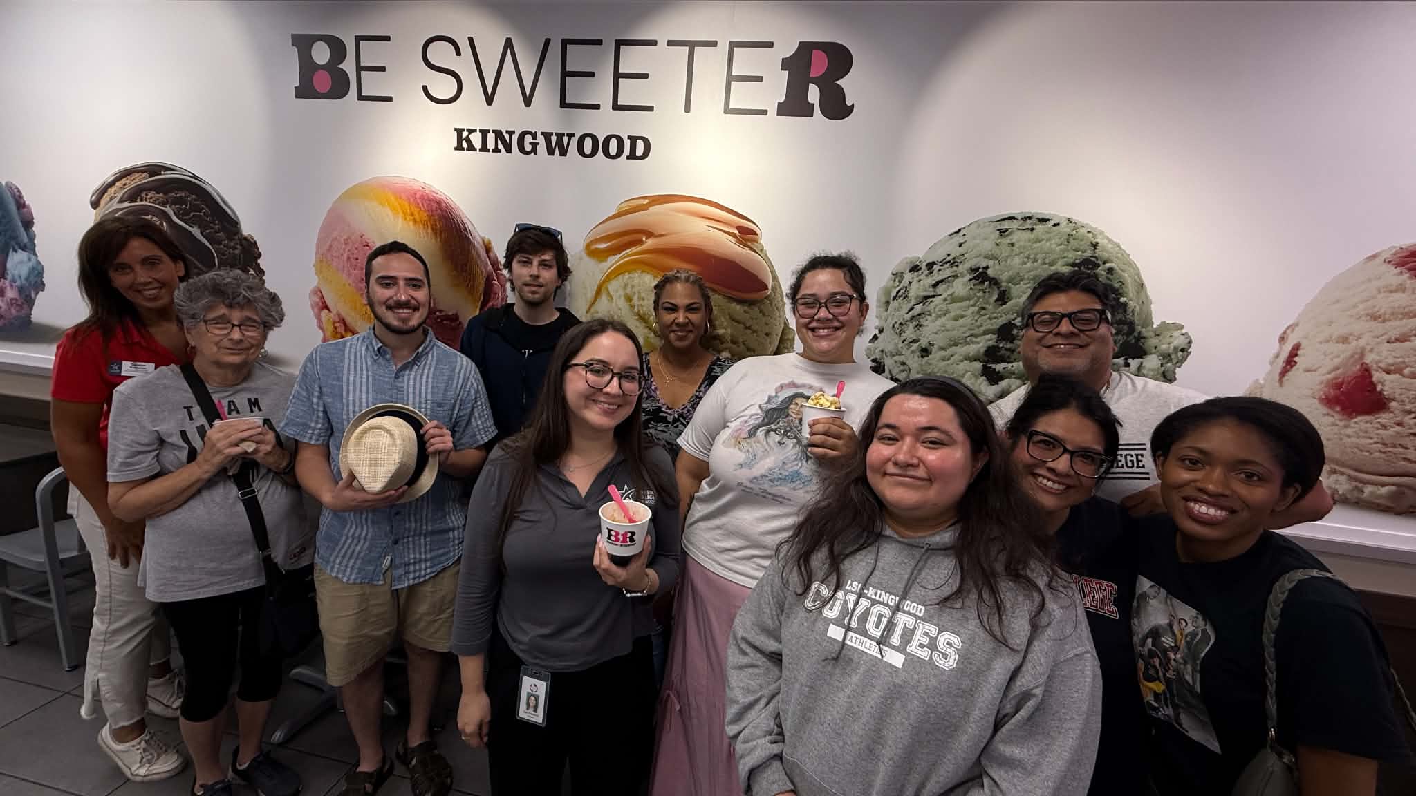 Group of alumni standing in front of a baskin robbins mural during an alumni pop up event.