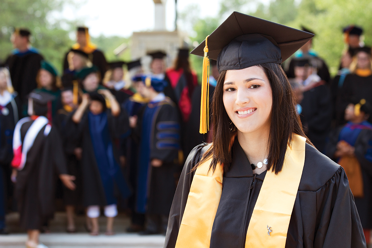 Graduate wearing regalia, with other graduates in background