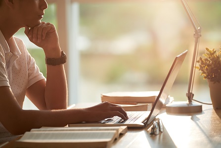 Photo of an individual sitting at a desk working on a laptop in a warmly lit room.