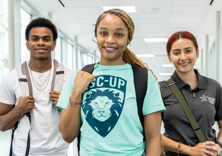 Group of Three Smiling Students in Hallway with Backpacks