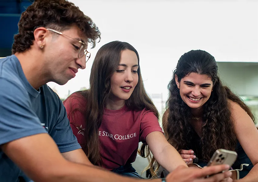 3 students smiling at a phone