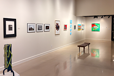 photo shot of second entrance of fine arts gallery with bench, ceramic sculpture and various photographs and paintings.