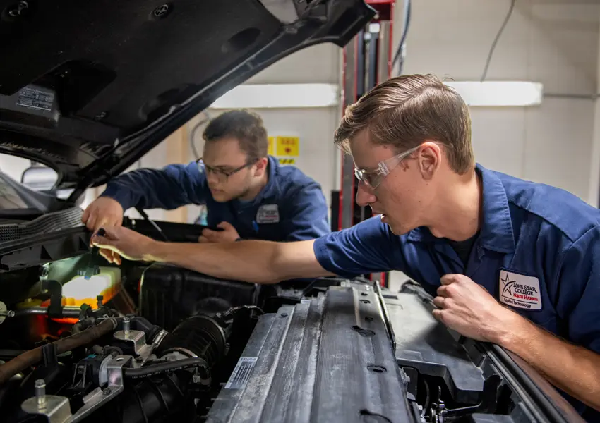 2 students checking the fluids under the hood of a car