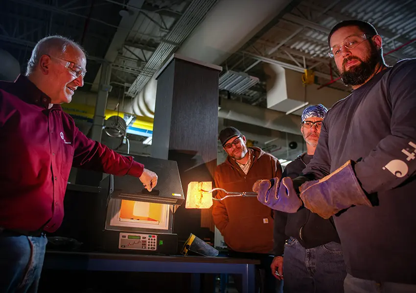 Female student sitting by desk using a ruler and holding a balde about to cut a printed poster