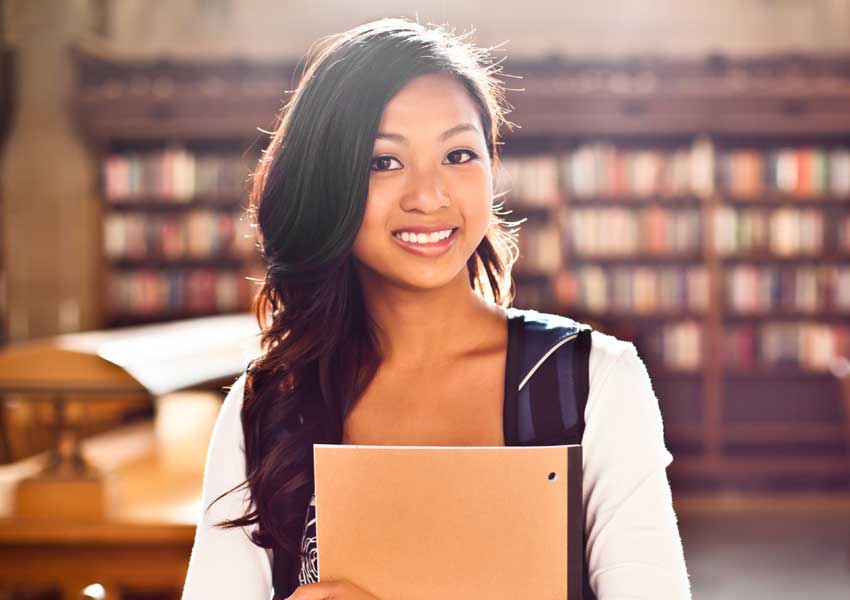 Girl smiling in a library holding a notebook.