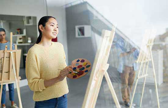 A women holding a palette while looking at a canvas