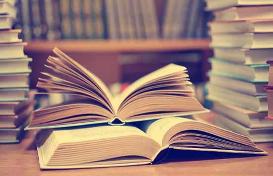 An open book surrounded by stacks of books