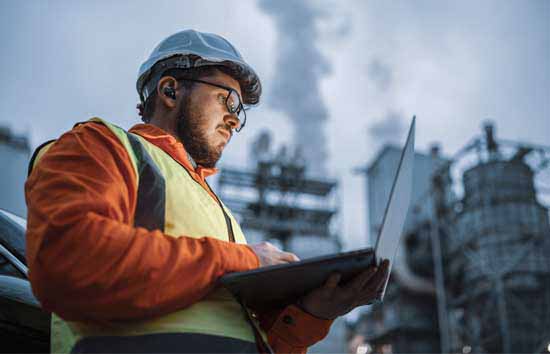 A man works on a laptop in front of industrial buildings