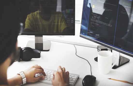 A man typing on a keyboard in front off 2 monitors