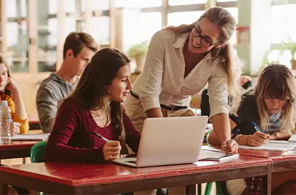 Teacher helping a student working on a laptop