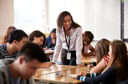 Teacher Standing By Student Table Teaching Lesson
