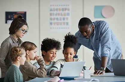 A teacher helps a group of students with a laptop