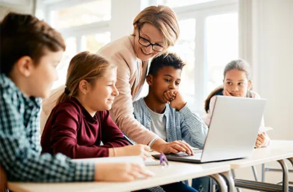 A teacher helps a group of students with a laptop